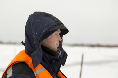 Mavi ceketli ve turuncu yelekli bir montajcının portresi.