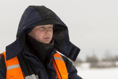 Mavi ceketli ve turuncu yelekli bir montajcının portresi.
