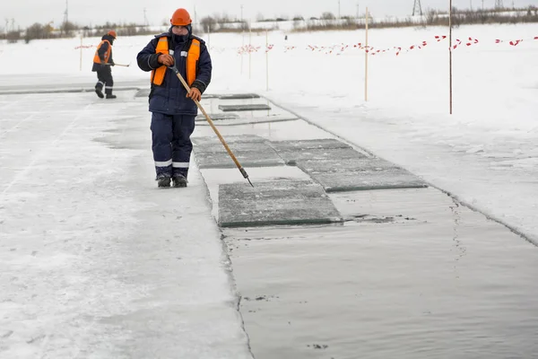 Arbetare flottar isblock längs en kanal ristade i en frusen sjö — Stockfoto