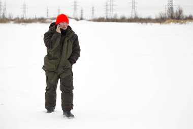 Donmuş bir gölün buzunda kırmızı şapkalı bir işçi, cep telefonuyla.