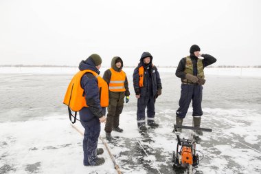 Bir patikanın yakınındaki donmuş göletin buzunda dört işçi.