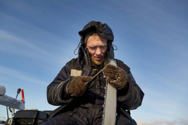 Mavi ceketli bir işçi elektrikli testereyi biler..
