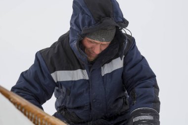 Builder on top of a snowy wall with a hacksaw in his hand