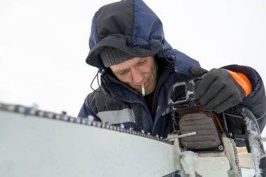 Mavi ceketli bir işçi elektrikli testereyi biler..