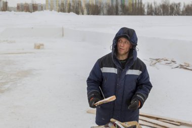Kışlık işçi tulumuyla elinde tahtasıyla.