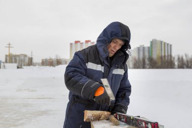 Worker in winter overalls with a hammer in his hand