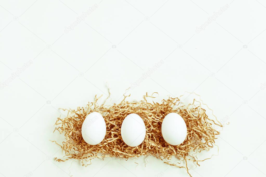 Three eggs on the straw on white background. Space for text.