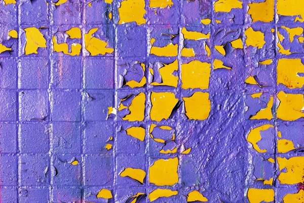 Painted shabby mosaic tiles on the facade of a house. Purple and yellow colors.
