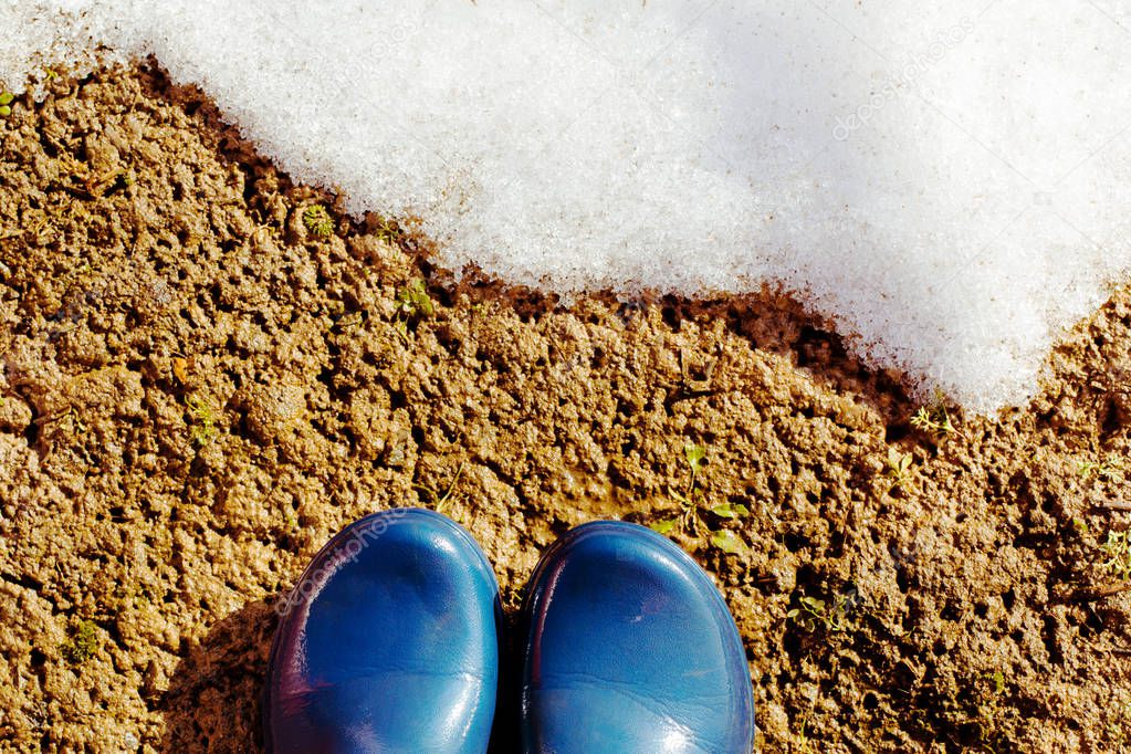 Blue rubber boots on the wet ground  in front of the melting snow. Sunny day.