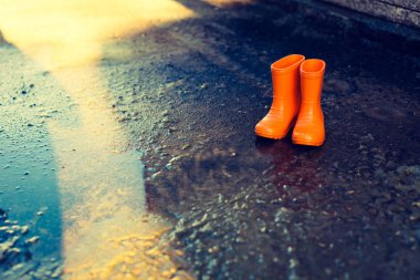 Su birikintisi ayakta turuncu lastik çizmeler.