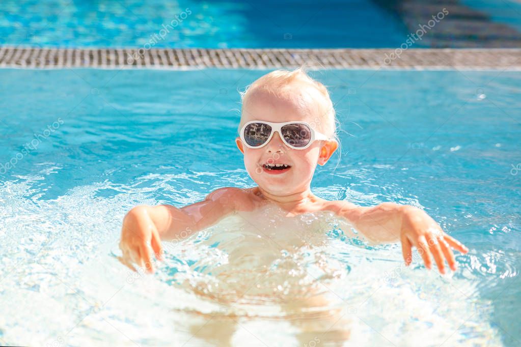 Cute little girl laughing and having fun splashing in the pool in the summer. 
