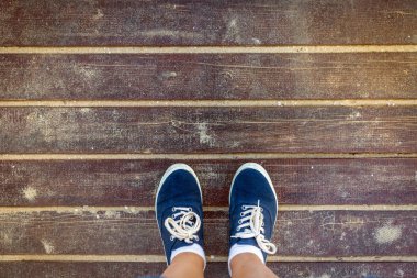 Eski kumlu ahşap zemin üzerinde duran mavi spor ayakkabıları. Üstten Görünüm.