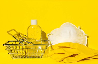Süpermarket alışveriş sepeti, N95 yüz maskesi, el koruma eldivenleri ve bir şişe jel dezenfektanı. Salgın sırasında markete gitmek için gerekli malzemeler. Bireysel koruma kavramı covid 19. 