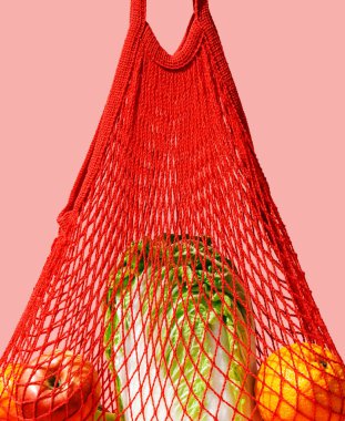 Pembe arka planda sebzeli ve meyveli kırmızı ip torbası. Sıfır atık, sağlıklı yaşam tarzı ve bilinçli tüketim kavramı.