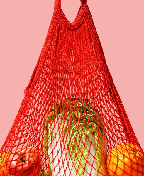 Red string bag with vegetables and fruit on a pink background. The concept of zero waste, healthy lifestyle and conscious consumption.