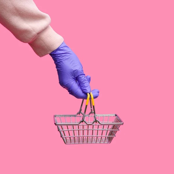 Tek kullanımlık parlak eldivenli bir kadının elinde pembe arka planda süpermarketten alınmış metal bir sepet var. Koronavirüs salgını sırasında müşterilerin güvenliği..