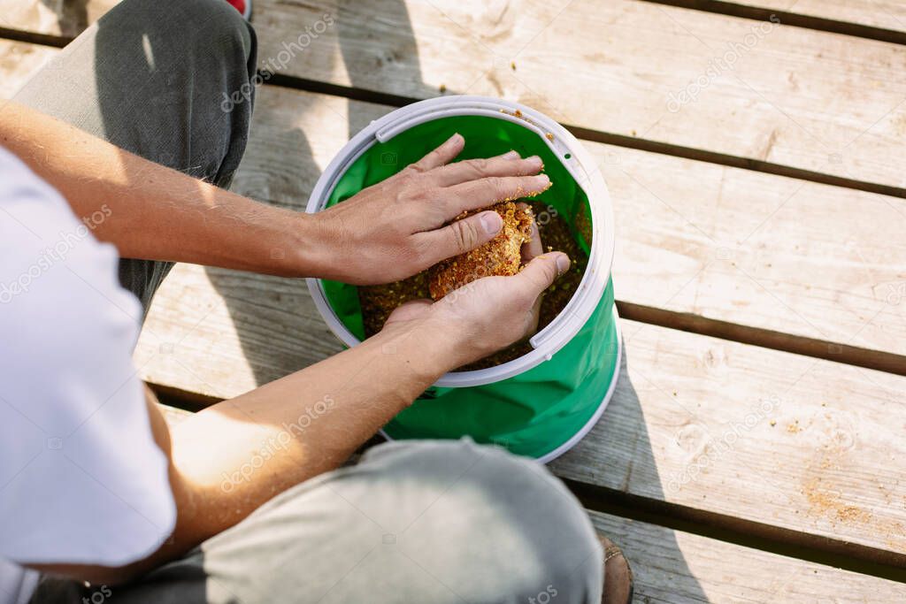 The fisherman picks up the bait for the fish from the bag. Hands close up