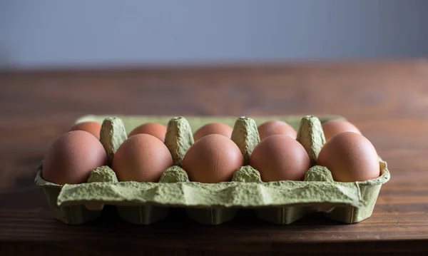 A carton of a dozen fresh eggs on wooden table