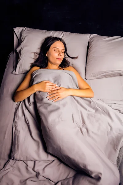 Woman sleeping in bed on a dark background.