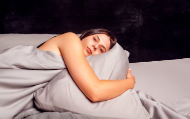 İçinde karanlık bir arka plan açık gözlerle yatakta yatan kadın.