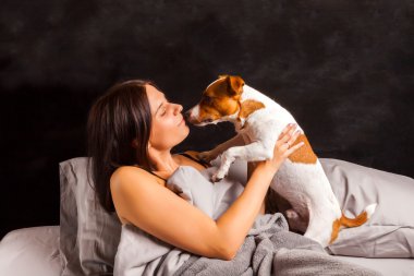 Genç güzel esmer kadın yatakta köpeğiyle oynuyor.