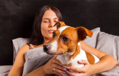 Genç güzel esmer kadın yatakta köpeğiyle oynuyor.