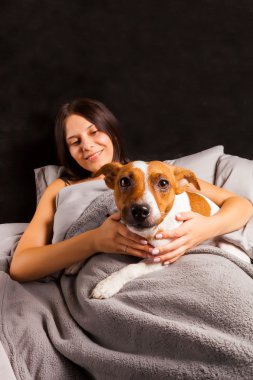 Genç güzel esmer kadın yatakta köpeğiyle oynuyor.