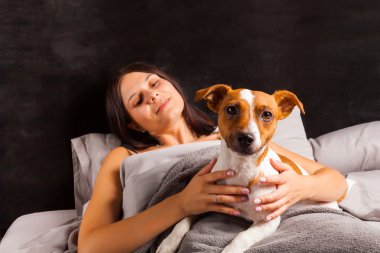 Genç güzel esmer kadın yatakta köpeğiyle oynuyor.