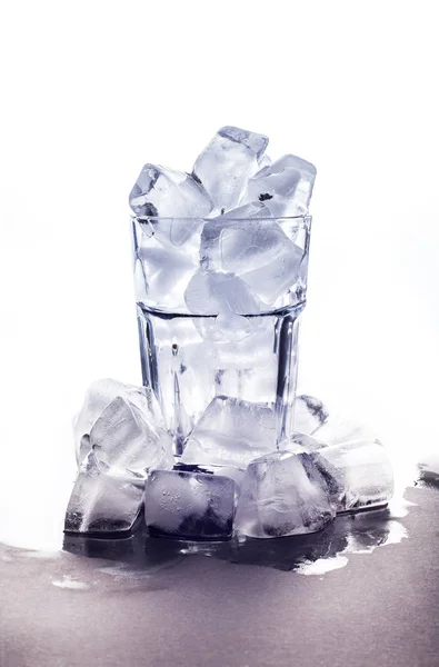 Glass with ice stands on a white background and pile of icicles at the bottom — Stock Photo, Image