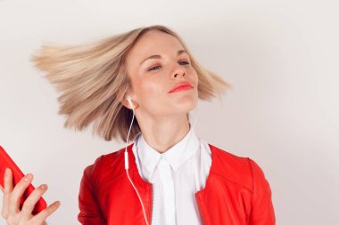 Kulaklıklar ve beyaz zemin üzerine kırmızı ceketli elinde cep telefonu ile bir kadın portresi