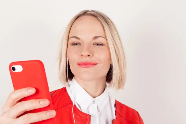 Portret kobiety z słuchawek i telefonu komórkowego w parze w czerwonej kurtce na białym tle — Zdjęcie stockowe