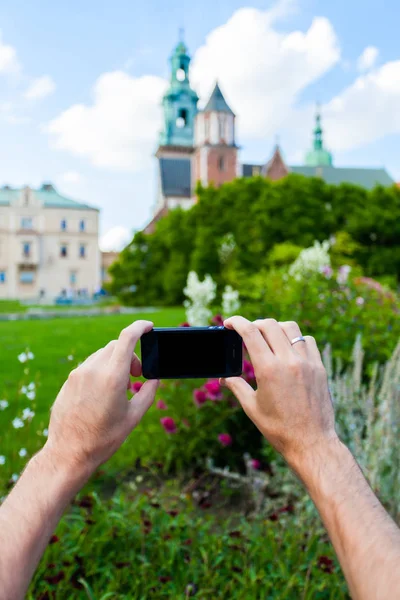 Um viajante do sexo masculino tira fotos em seu telefone celular contra o fundo do Castelo Wawel — Fotografia de Stock