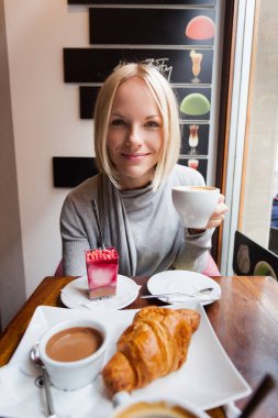 Genç kadın sabah kruvasan ve hafif köpük tatlı kahve içer