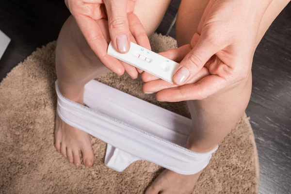 Woman is sitting on the toilet and holding a positive pregnancy test