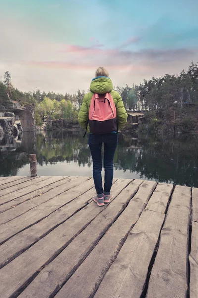 Ένα γυναικείο ταξιδιώτη στέκεται σε μια ξύλινη αποβάθρα κοντά σε μια όμορφη λίμνη σε ένα πευκόφυτο δάσος. — Φωτογραφία Αρχείου