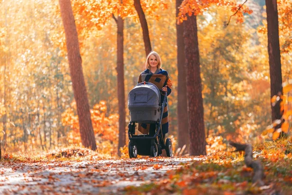 Una joven madre con un cochecito pasea por el parque de otoño — Foto de Stock