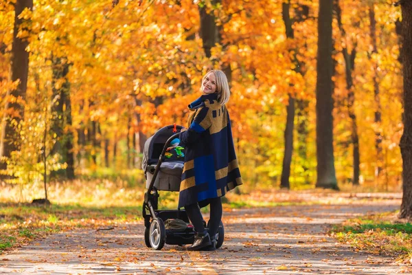Una joven madre con un cochecito pasea por el parque de otoño — Foto de Stock