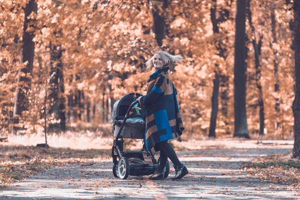 Une jeune mère avec une poussette marche à travers le parc d'automne — Photo