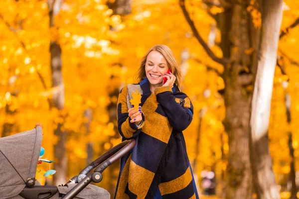 Mladá matka s kočárek mluví na její mobilní telefon na procházce v parku — Stock fotografie