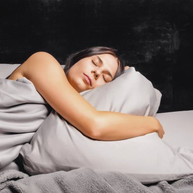 Karanlık bir arka plan üzerinde yatakta uyuyan kadın.