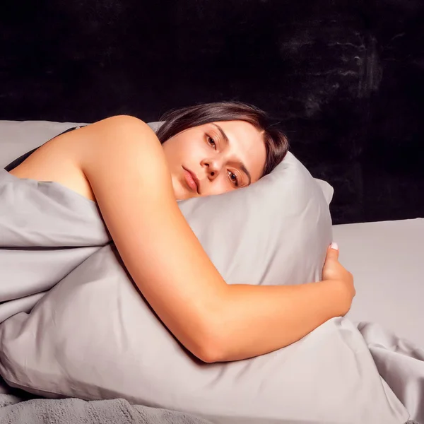 Mujer acostada en la cama sobre un fondo oscuro con los ojos abiertos . — Foto de Stock