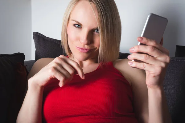 Bir kadın akşam kanepede yatıyor ve bir cep telefonu tutan — Stok fotoğraf