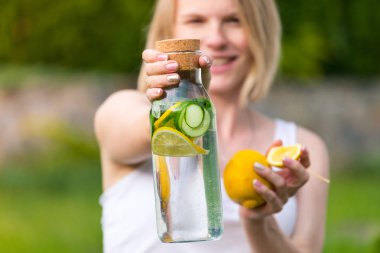 Kız bir detoks içecek bir limon ve nane bir salatalık ile yeşil çim bir arka plan üzerinde tutuyor