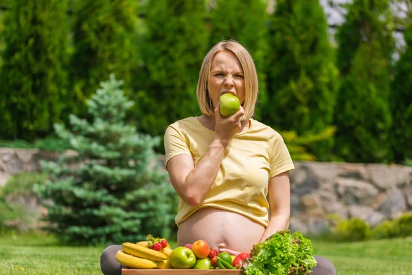 Έγκυος γυναίκα κάθεται στο γρασίδι και κρατώντας ένα μήλο στο χέρι — Φωτογραφία Αρχείου