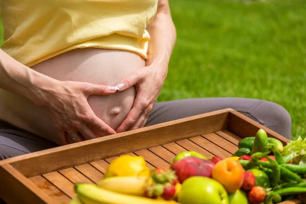 Беременная женщина сидит на траве и держит яблоко в руке — стоковое фото