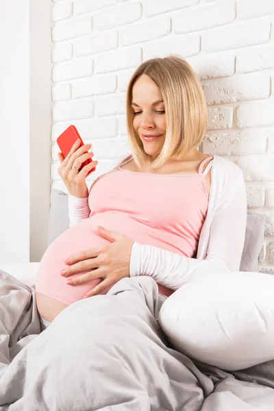 幸せな笑顔の妊婦ベッドに位置し、携帯電話で見える — ストック写真