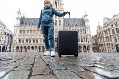 Belçika, Brüksel 'deki Grand Place' e elinde bavulla giden bir kadın turist.