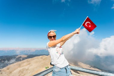 Genç kadın turist, Kemer 'deki Tahtali Dağı' nın izleme platformunda elinde kırmızı hindi bayrağıyla duruyor, Türkiye