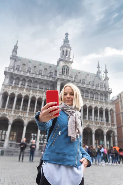 Una mujer toma fotos en su teléfono con el telón de fondo del Museo de la Ciudad de Bruselas en la plaza principal Grand place en Bruselas, Bélgica — Foto de Stock