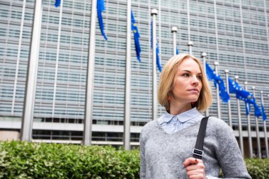 A young woman stands against the backdrop of the European Commission headquarters in Brussels, Belgium clipart